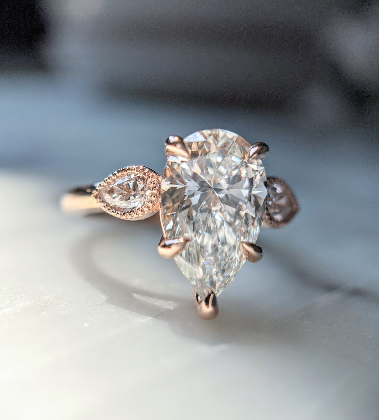 Pear shaped diamond engagement ring with pear side stones in milgrained bezels