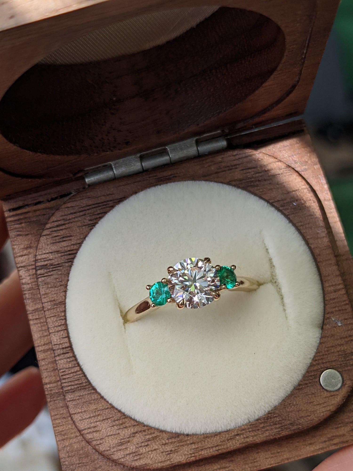Round diamond engagement ring with round emerald side stones.  Set in yellow gold.